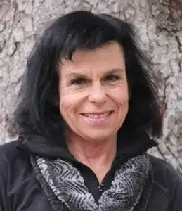 A woman with black hair and a scarf is smiling in front of a tree.
