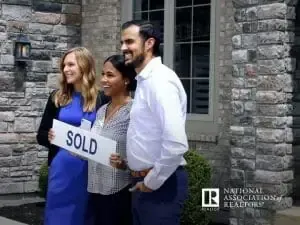 A group of people standing in front of a house holding a sold sign.