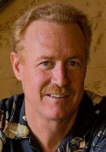 A man with a mustache and a blue shirt is smiling for the camera.