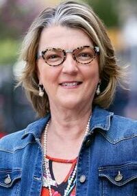 A woman wearing glasses and a denim jacket is smiling for the camera.