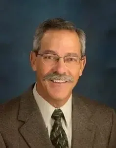 A man with a mustache and glasses is wearing a suit and tie.