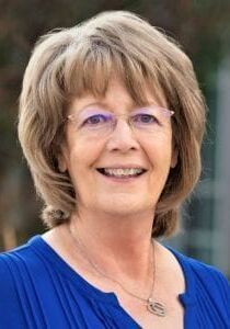 A woman wearing glasses and a blue shirt is smiling for the camera.