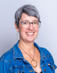 A woman wearing glasses and a denim jacket is smiling for the camera.