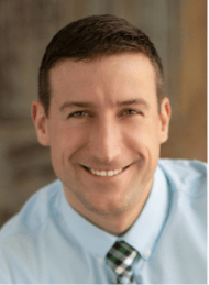 A man in a blue shirt and tie smiles for the camera