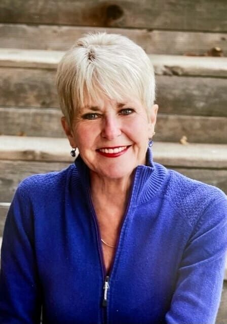 A woman in a blue sweater is smiling for the camera while sitting on a bench.