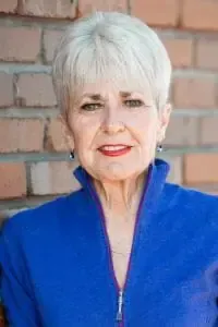 A woman in a blue jacket is standing in front of a brick wall.