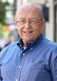 An older man wearing glasses and a blue shirt is smiling for the camera.