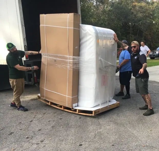 Workers loading a large boxed machine on a pallet outside a warehouse