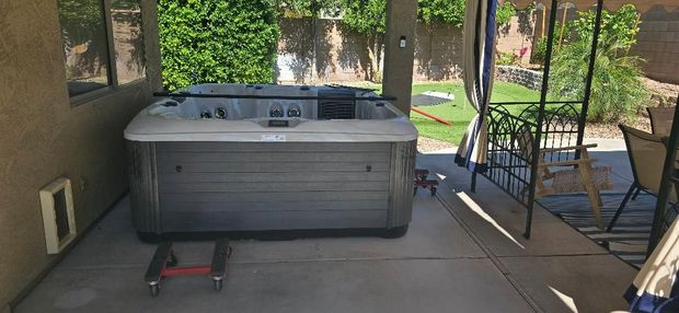 Hot tub on a patio beside a house, with a red dolly in front and a covered walkway nearby