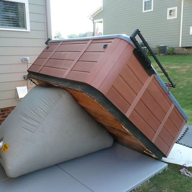 Collapsed red-brown hot tub leaning onto a gray covered object on a patio beside a house