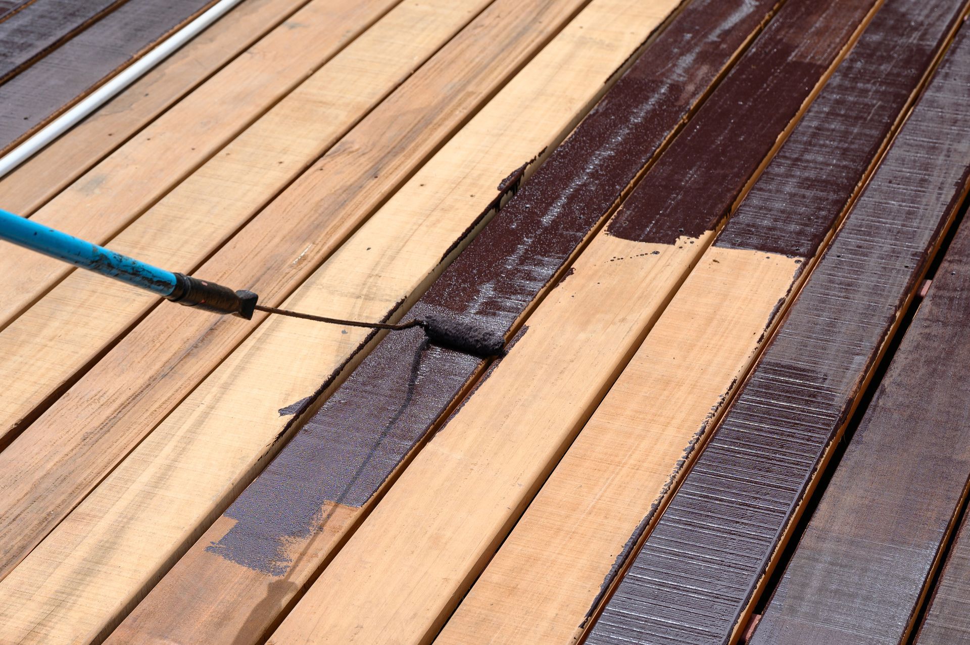 A person is painting a wooden deck with a roller.