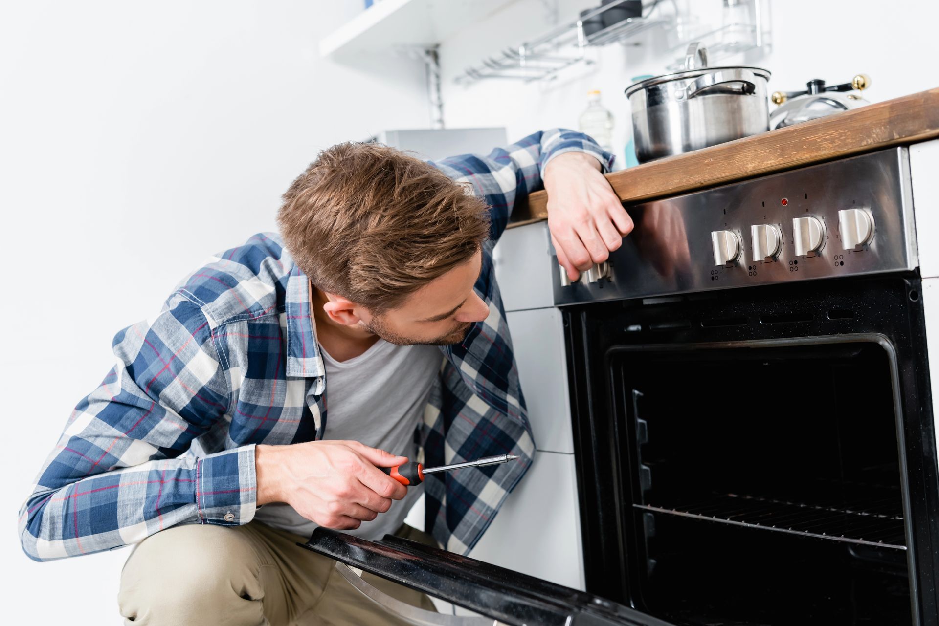 A man is fixing an oven with a screwdriver in a kitchen.