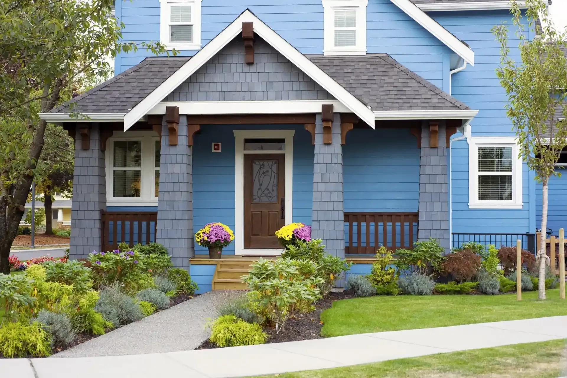 A blue house with a porch and flowers in front of it