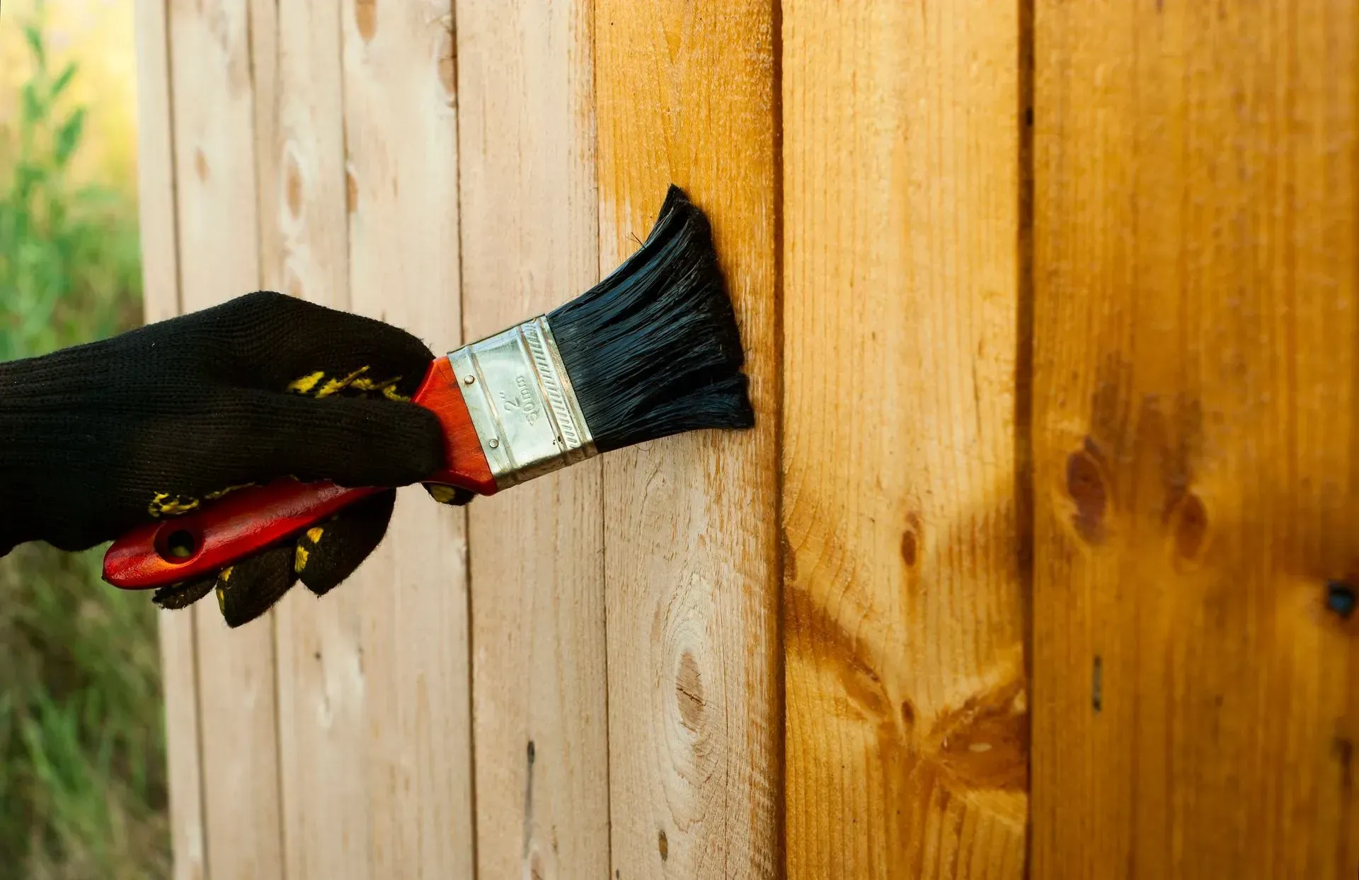 A person is painting a wooden fence with a brush.