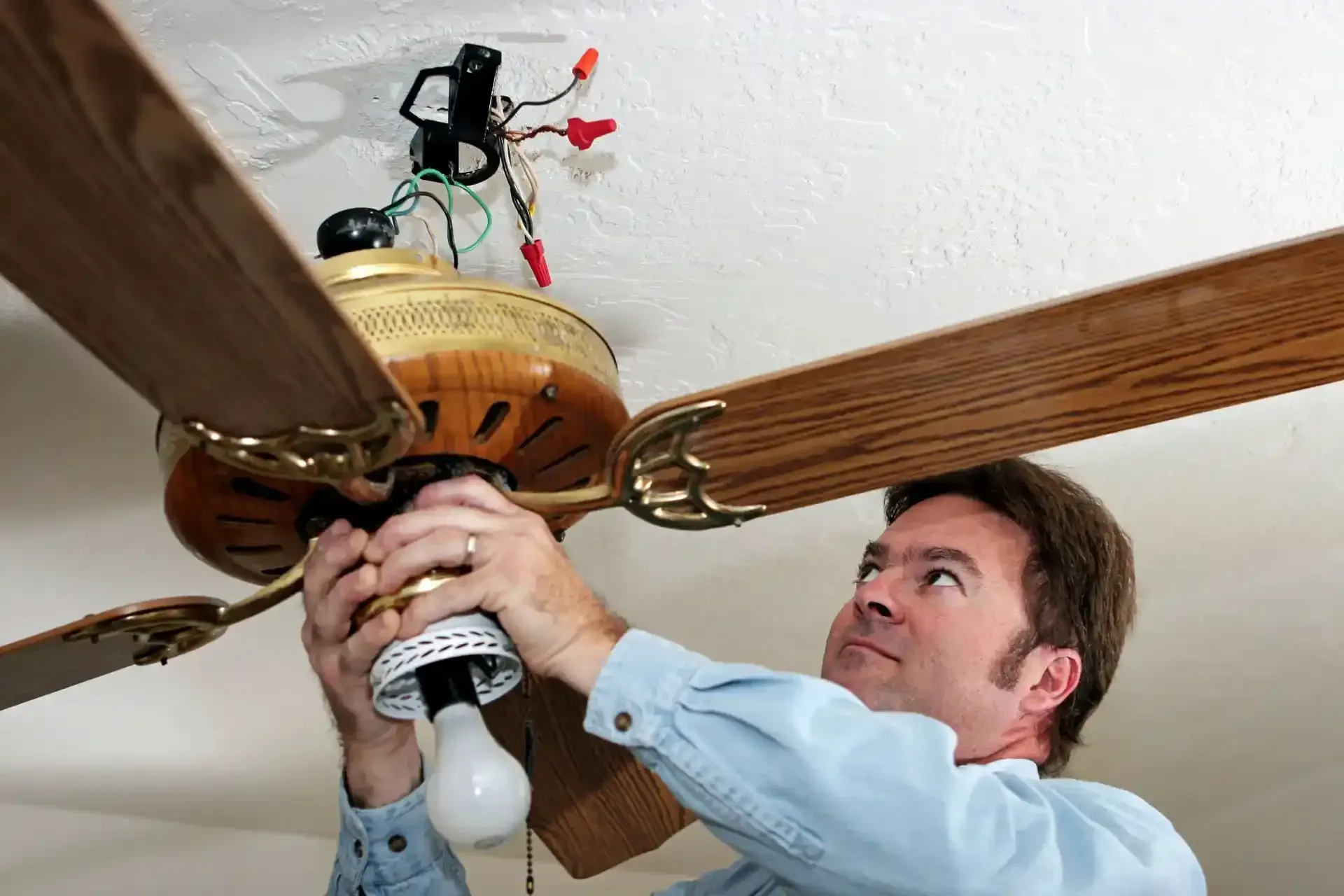 A man is fixing a ceiling fan with a light bulb.