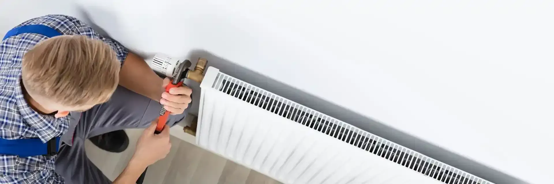 A man is fixing a radiator with a wrench.