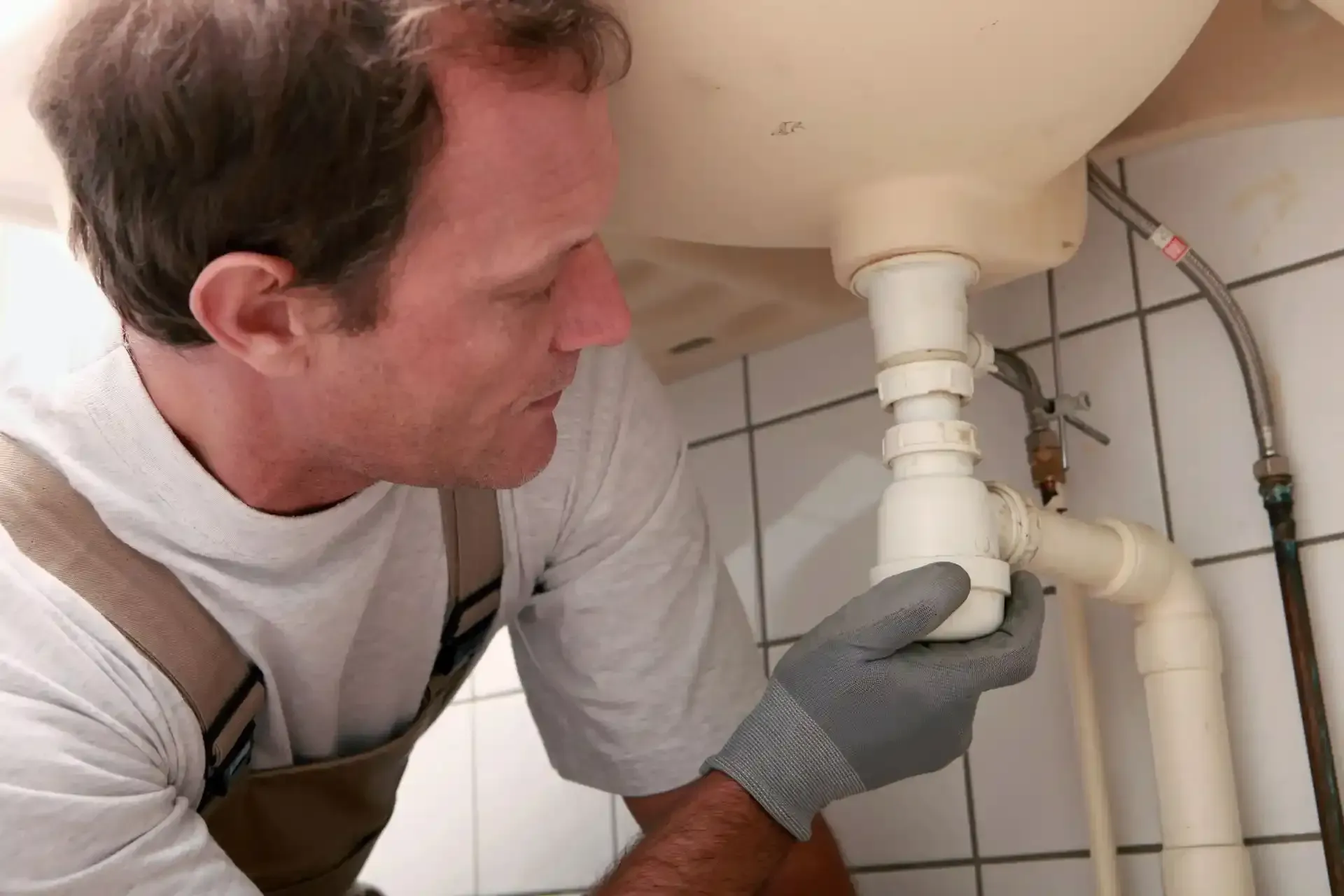 A man is fixing a sink pipe in a bathroom.