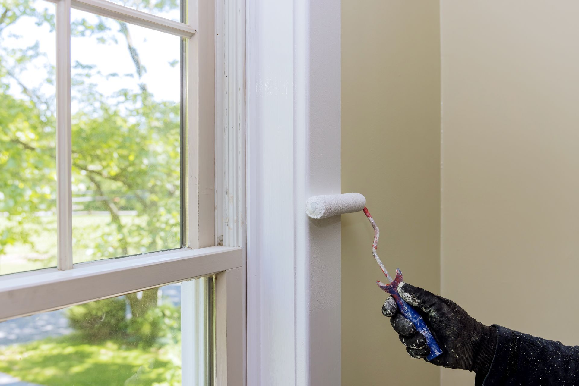 A person is painting a window frame with a roller.