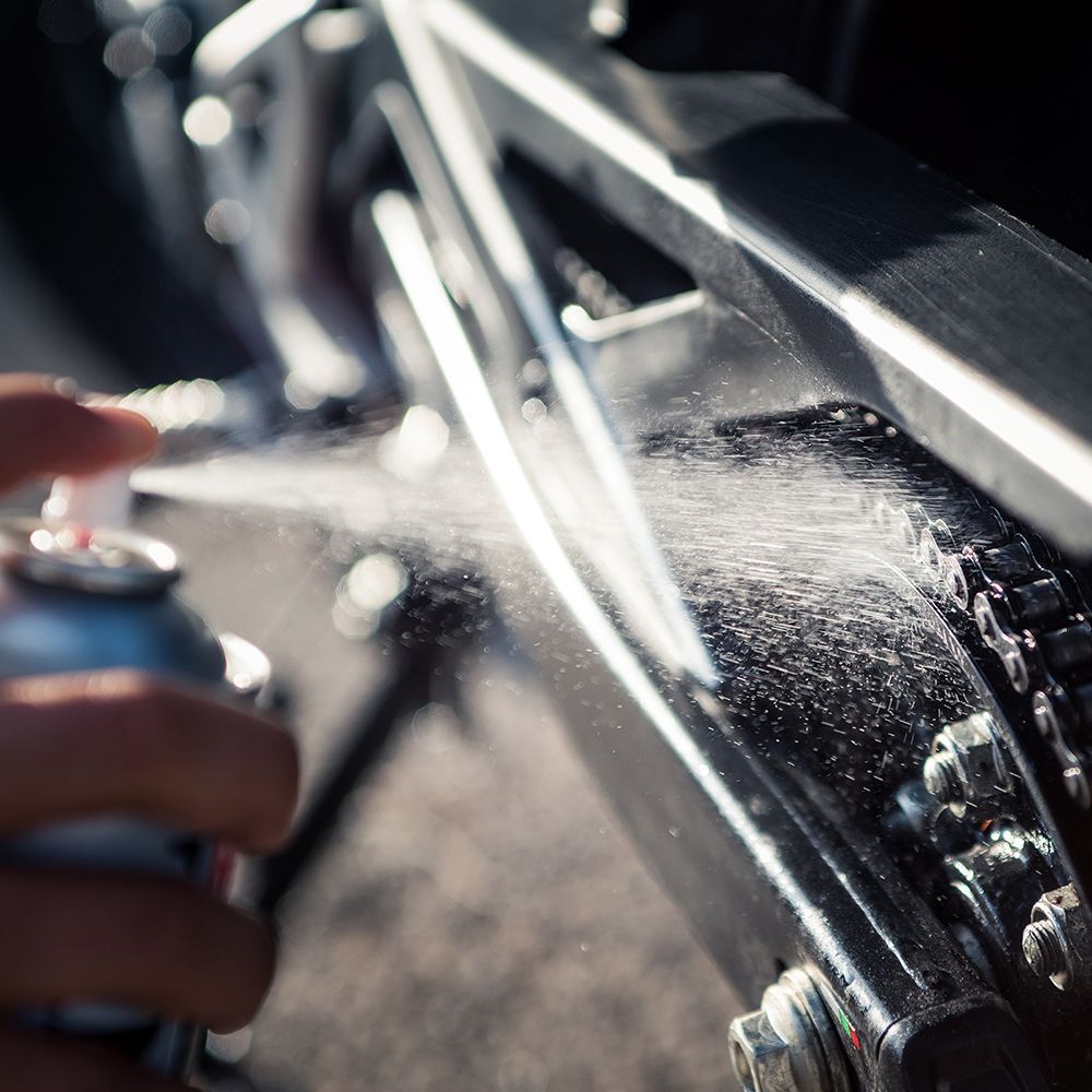a person is spraying a can of lubricant on a motorcycle chain