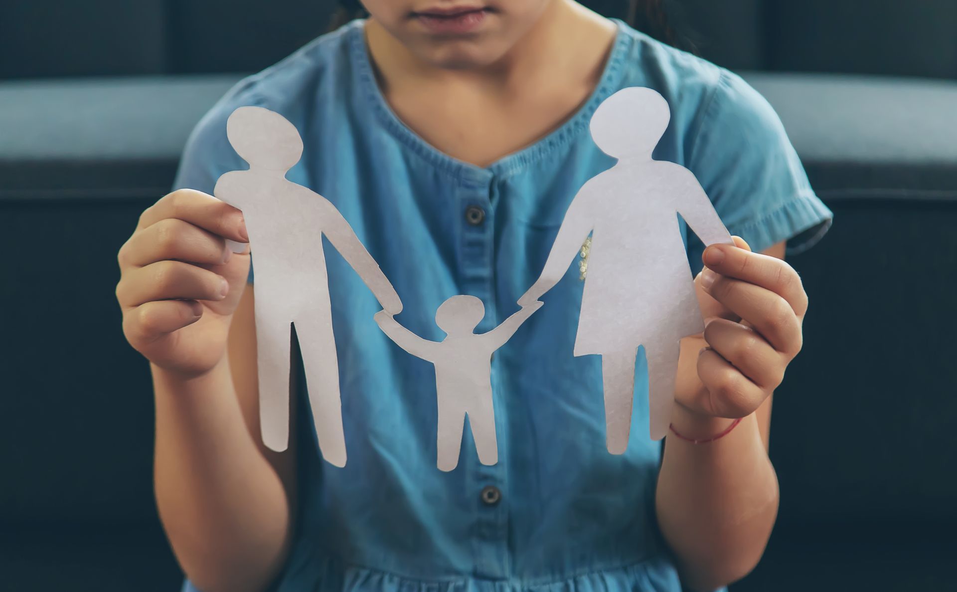 A child holding a paper cutout of two parents and a child holding hands.