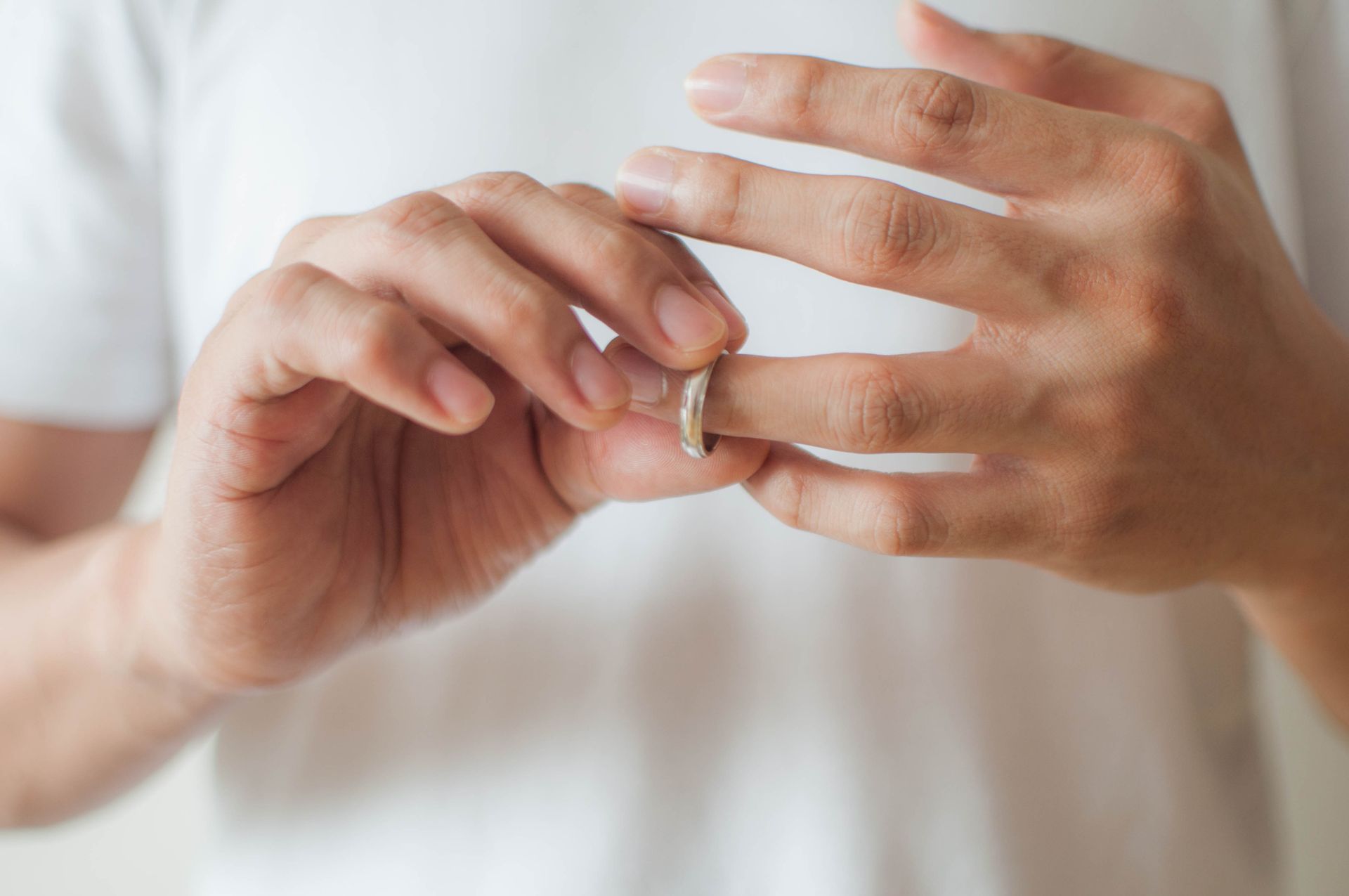 Person removing a wedding ring, hands close-up, white shirt, neutral background.