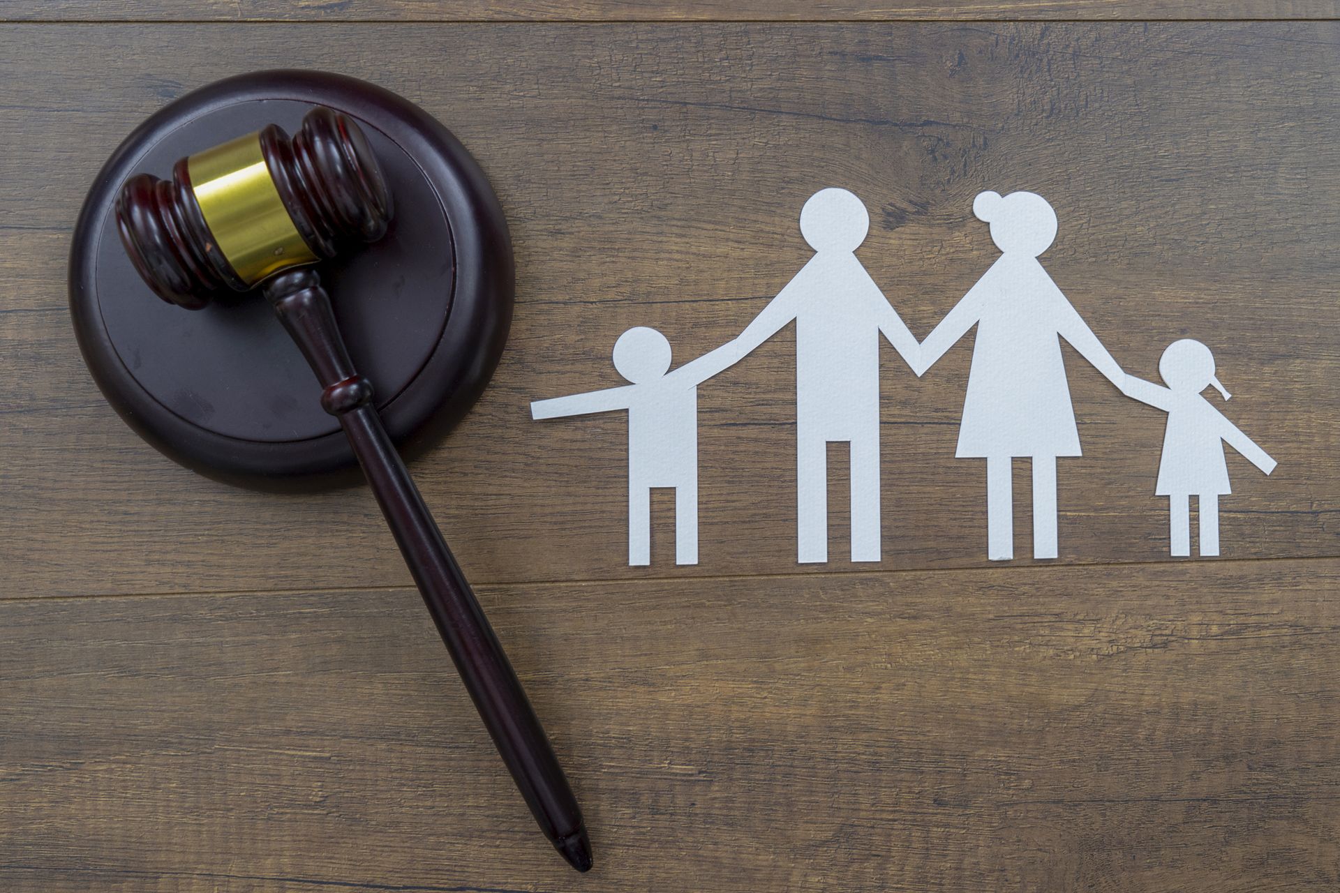 Gavel beside a paper cut-out family on a wooden surface; legal and family concept.