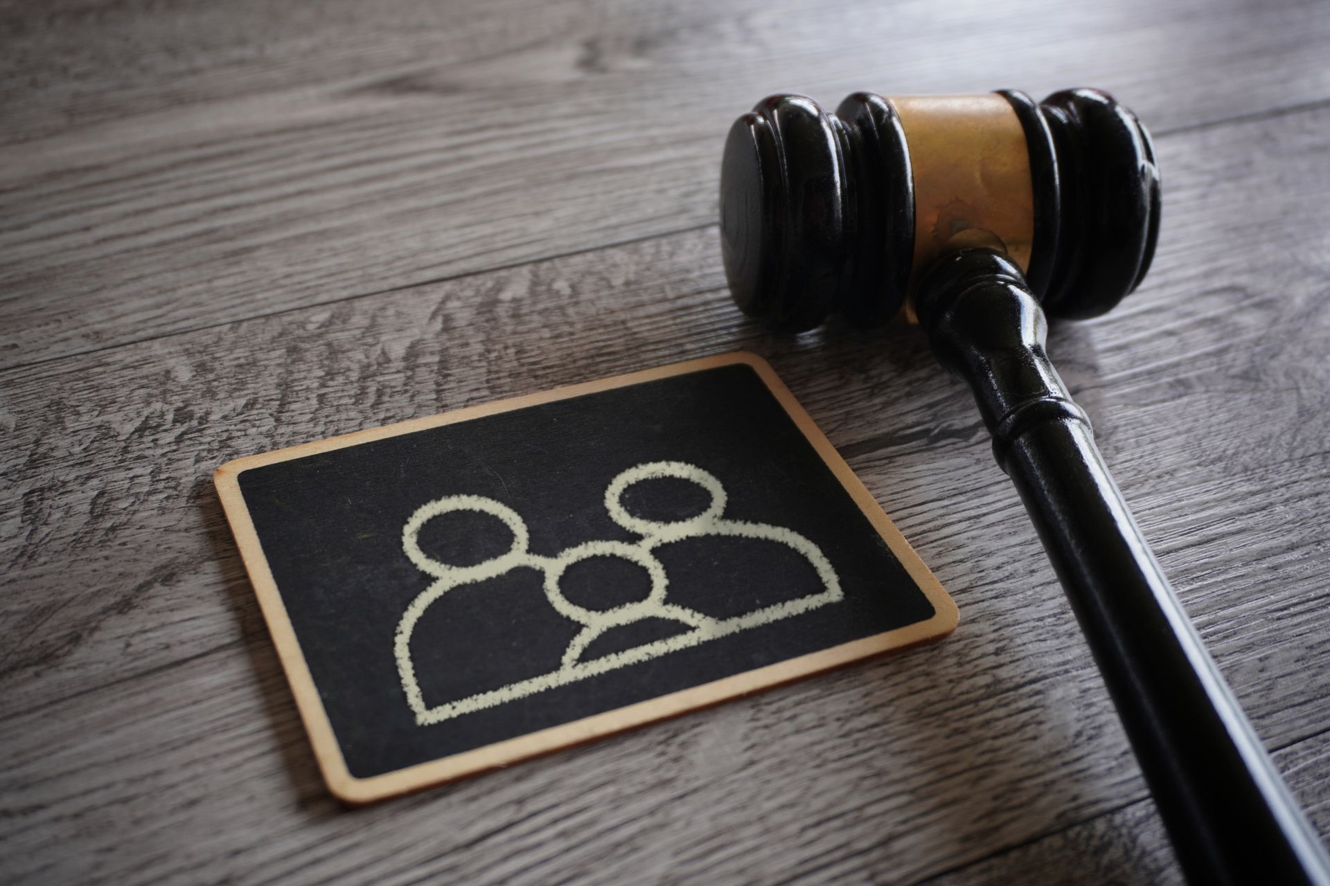 Black gavel next to a chalkboard with a family illustration on a wood surface.