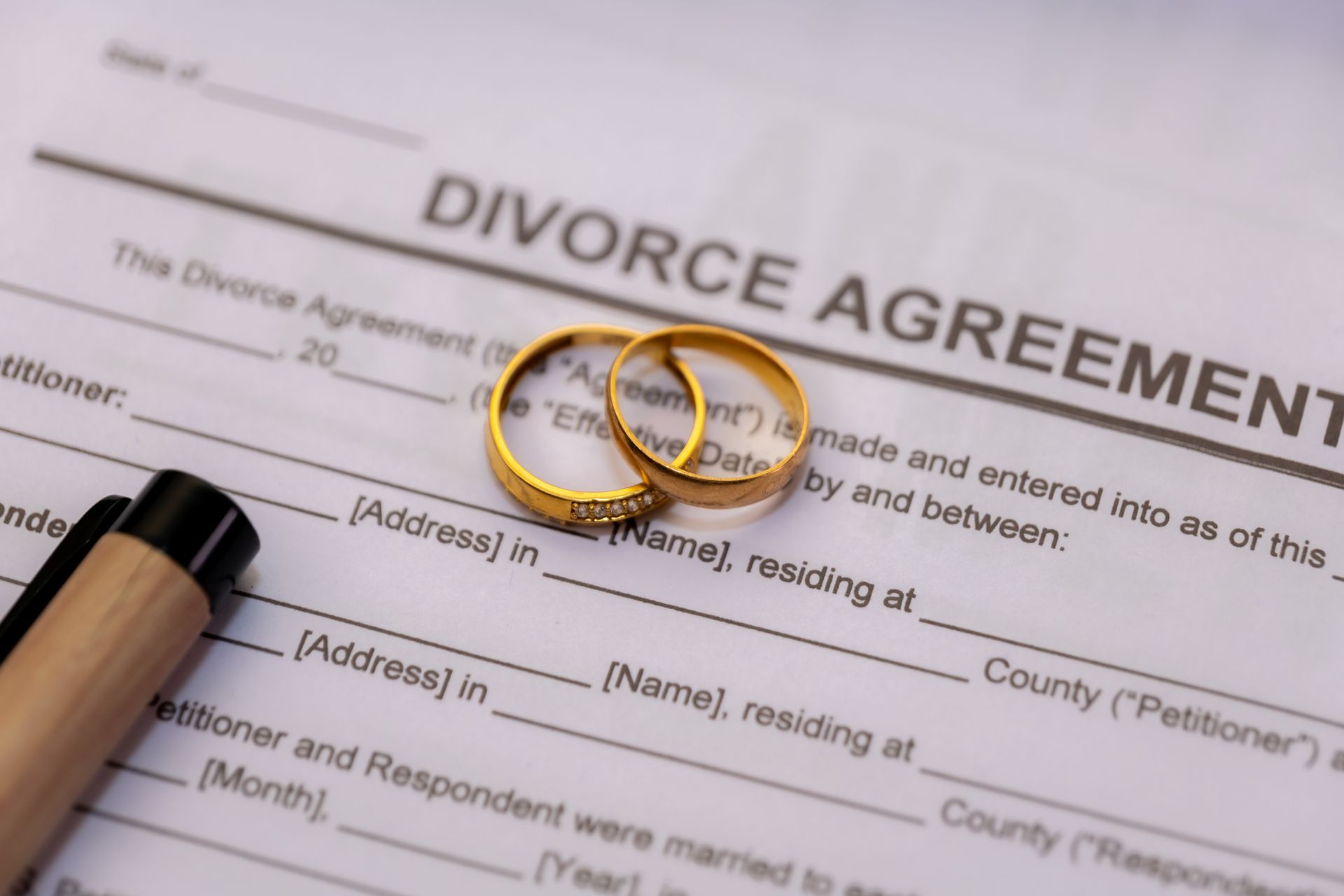 Two gold wedding rings on a divorce agreement document, with a pen.