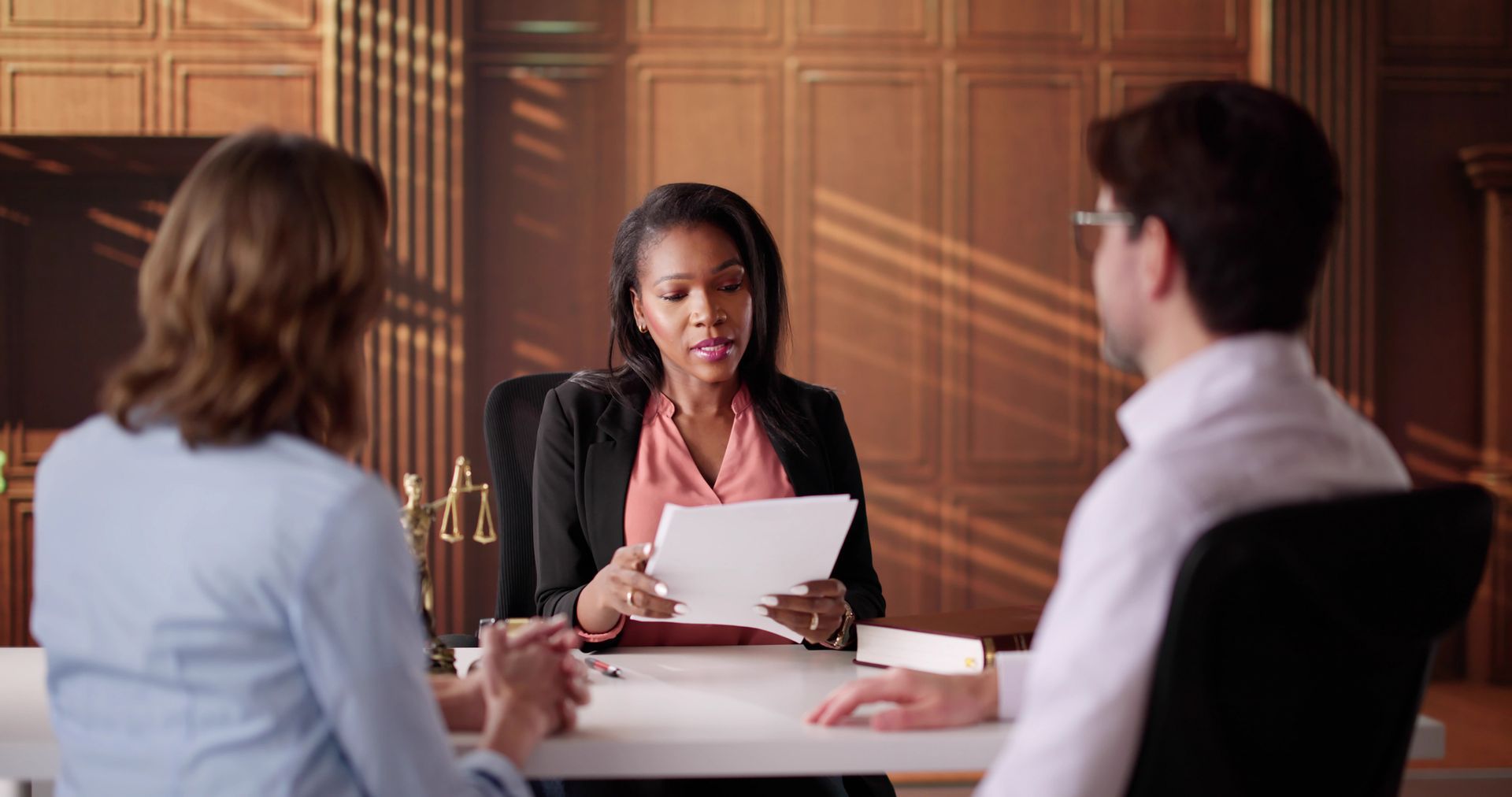 A Black woman lawyer reviews documents with a couple in a law office.