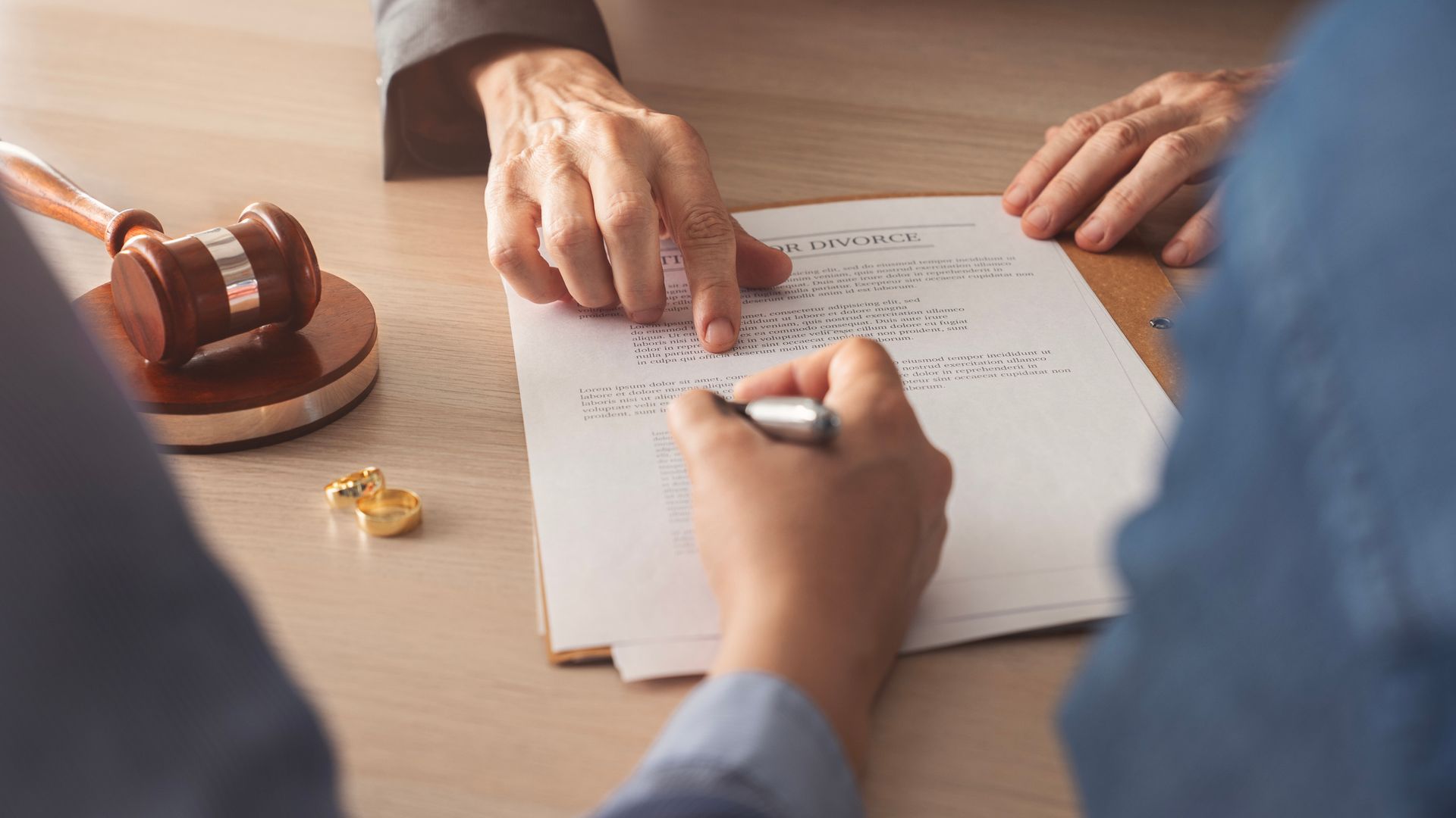 Hands pointing at and signing a legal document with a gavel and gold object on a desk.