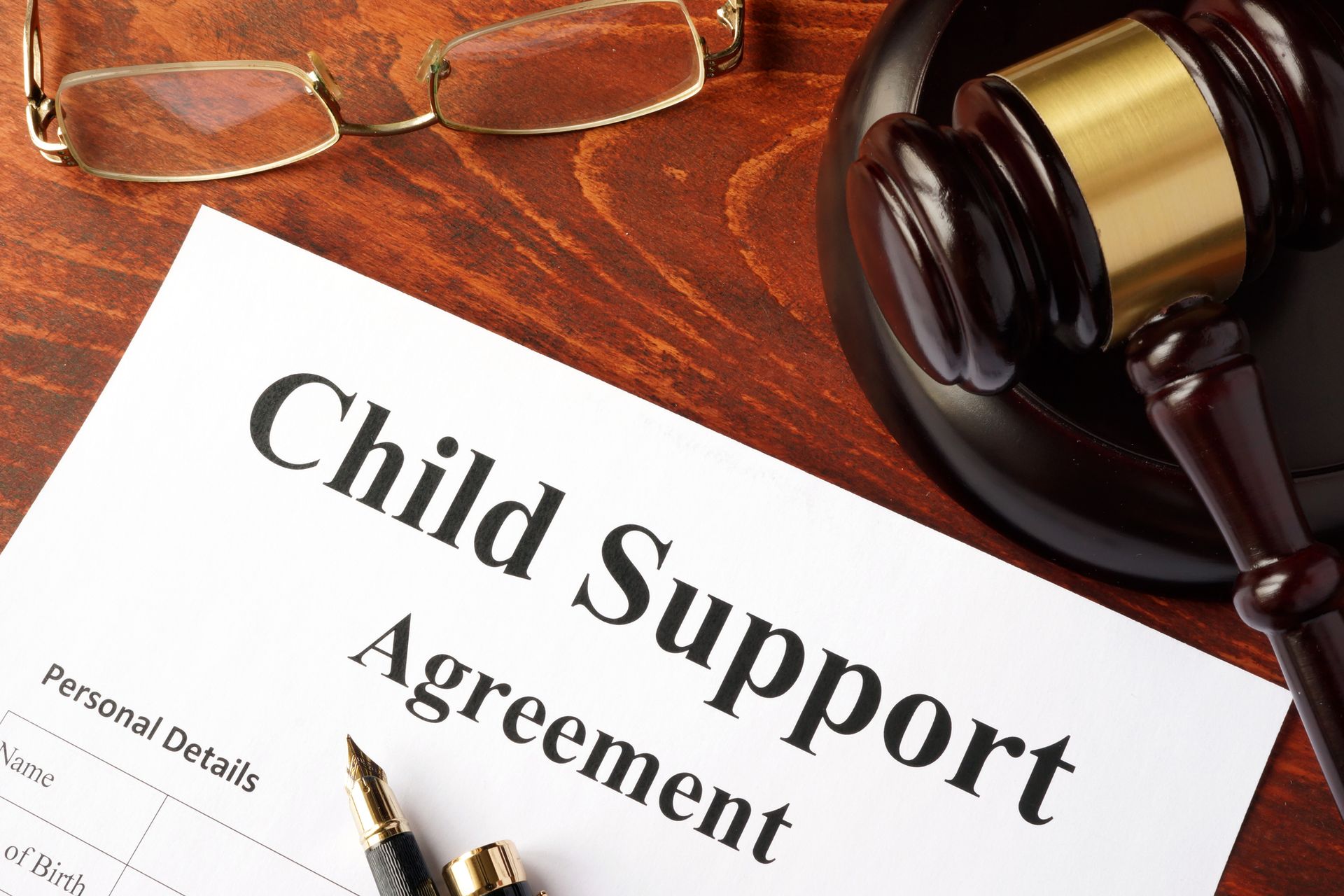 Child Support Agreement document with a gavel, pen, and glasses on a wooden table.