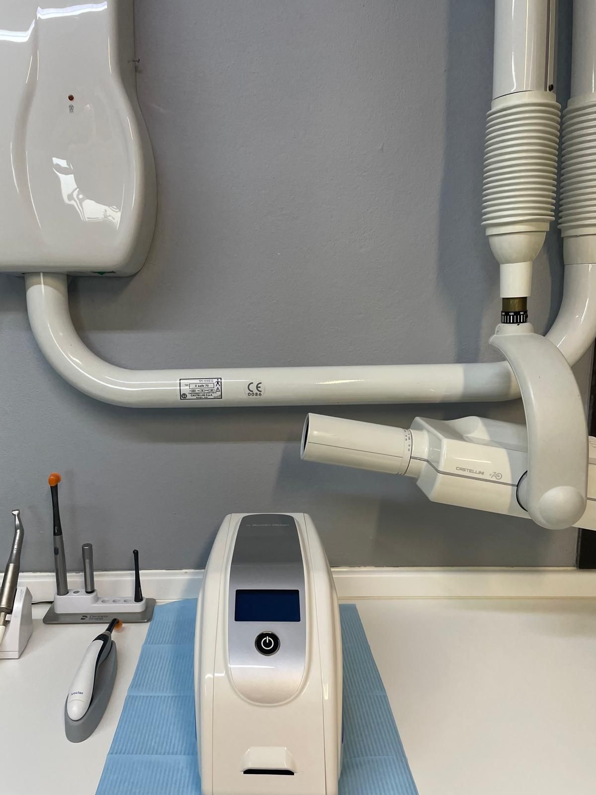 Apparecchio radiologico dentale con braccio bianco, posizionato su un piano di lavoro. Attrezzi e materiali sono disponibili nelle vicinanze.