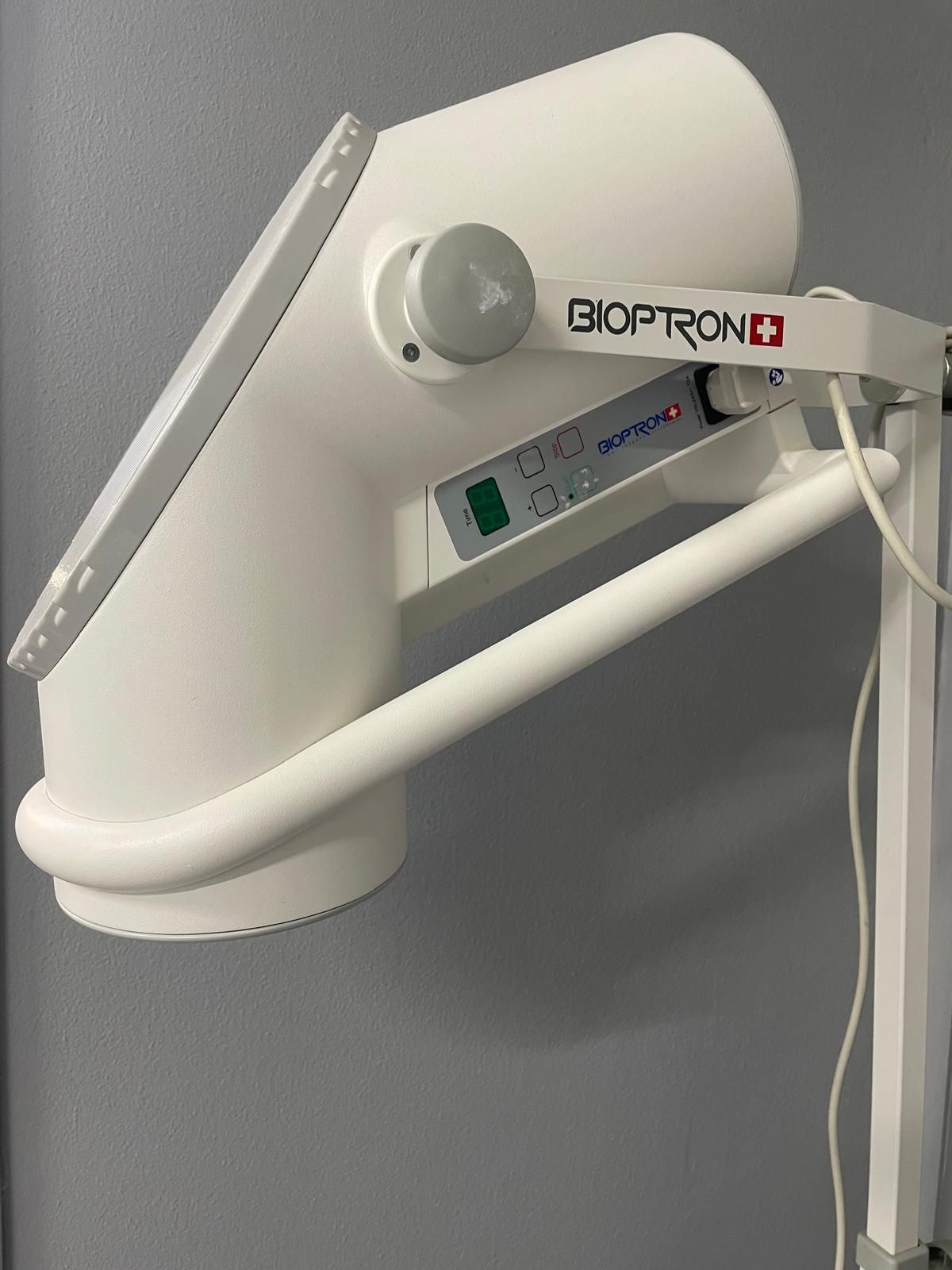 Dispositivo per la fototerapia Bioptron bianco montato su un supporto contro una parete grigia.