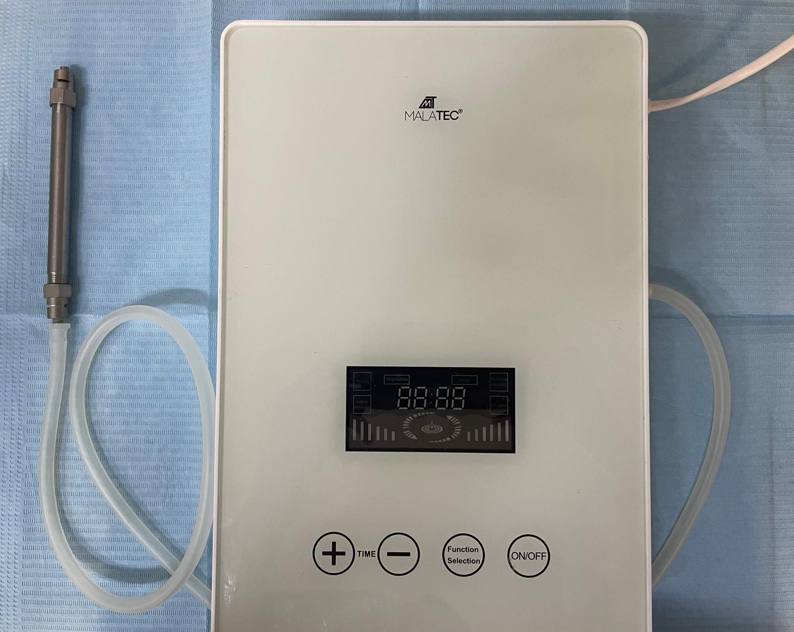 Purificatore d'acqua bianco con display digitale e pulsanti più/meno, tubi e ugello metallico su un panno blu.