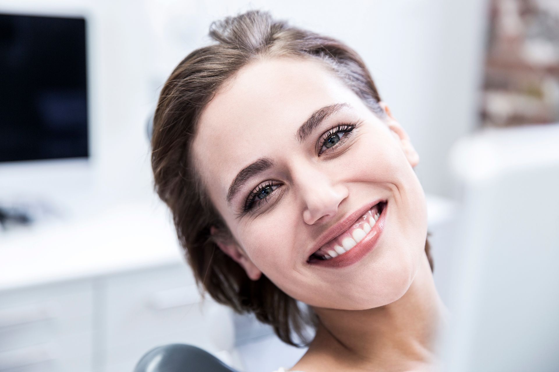 Ragazza sorridente sulla poltrona del dentista, con sedia blu e bavaglino protettivo.