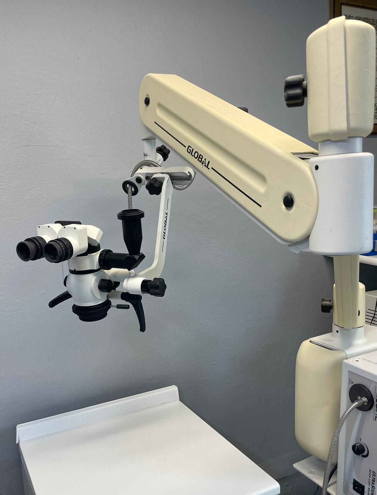 Braccio del microscopio medico con oculari, montato su un supporto bianco nello studio di un medico.