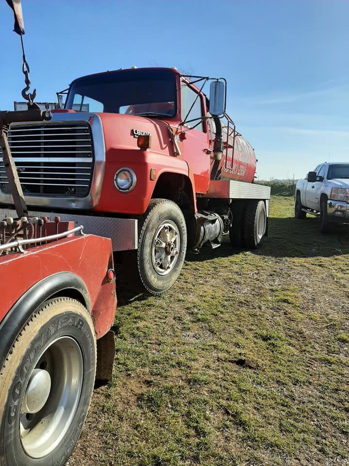 A red tow truck is being towed by a white truck in a field.