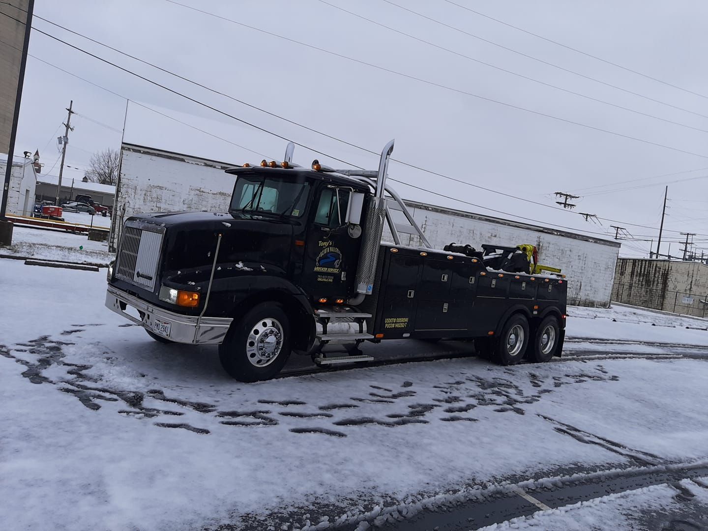 A black tow truck is parked in the snow in front of a building.
