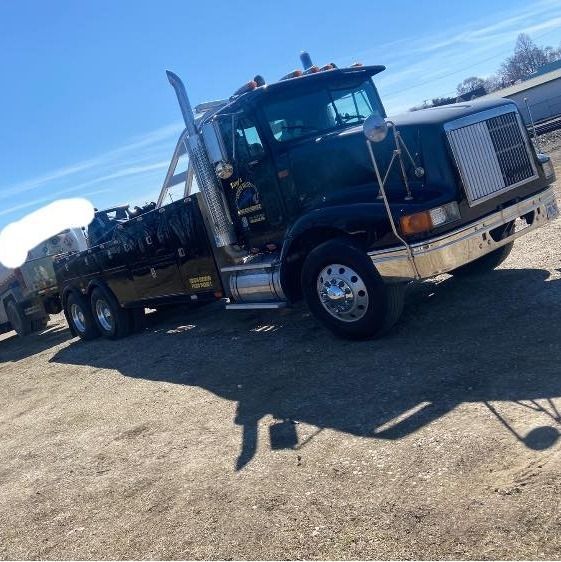 A black tow truck is parked on a dirt road