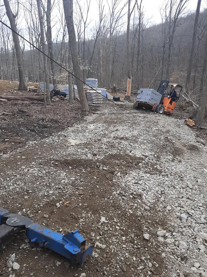 A forklift is driving down a dirt road in the woods.