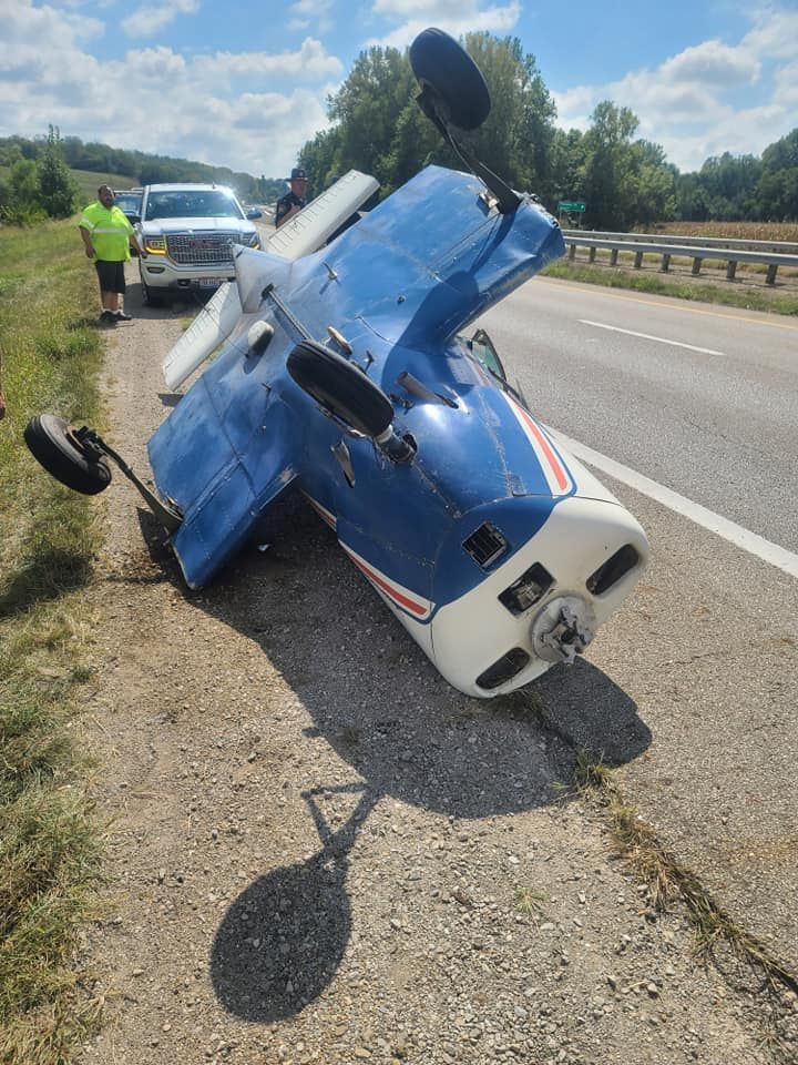 A small plane is laying on its side on the side of the road.