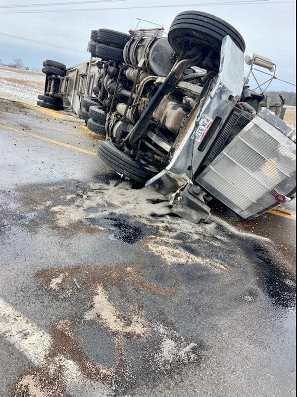A semi truck is turned over on its side on the side of the road.