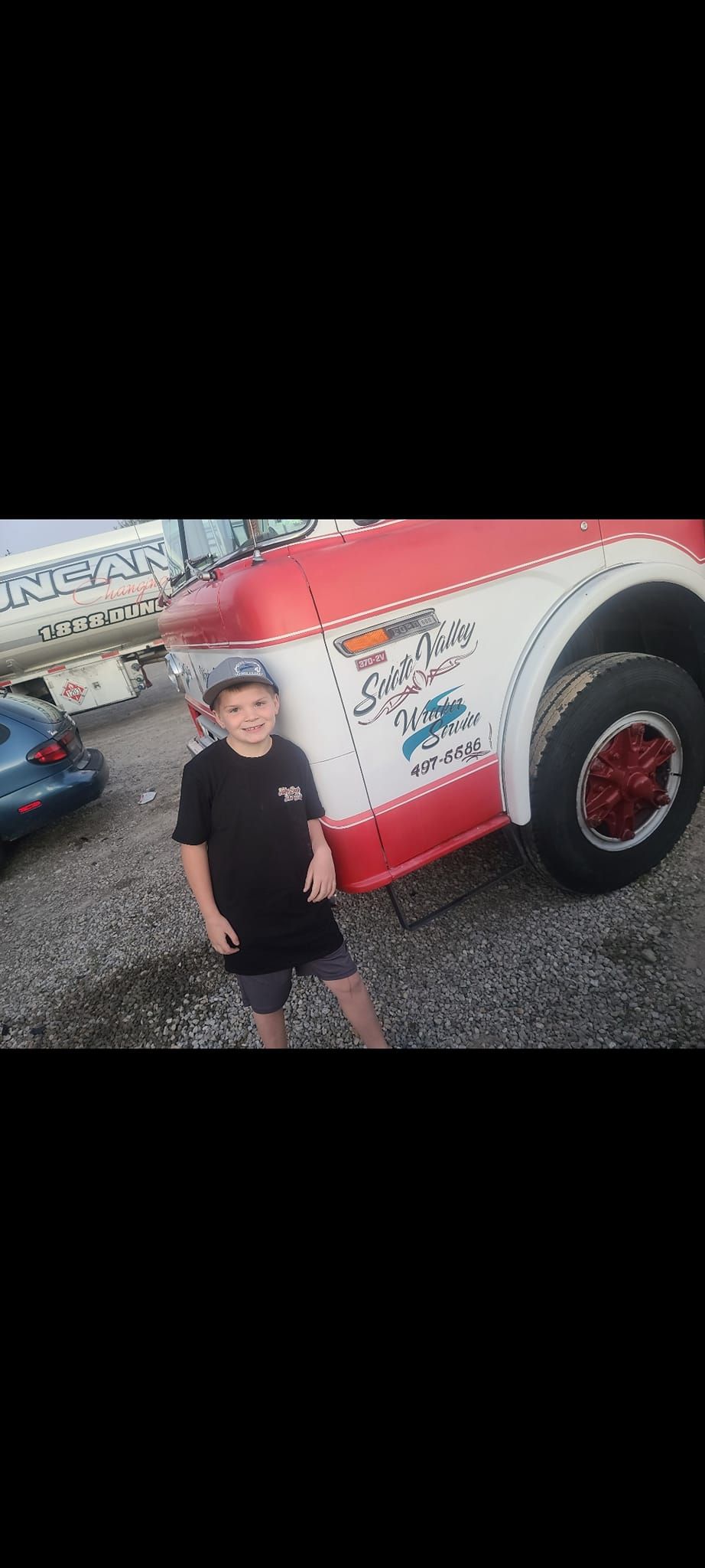 A young boy is standing in front of a red and white truck.