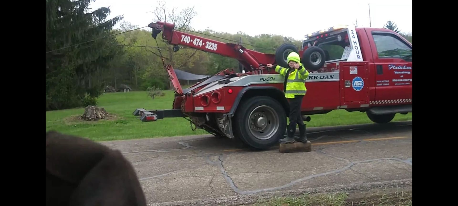 A man in a yellow vest is standing next to a red tow truck.