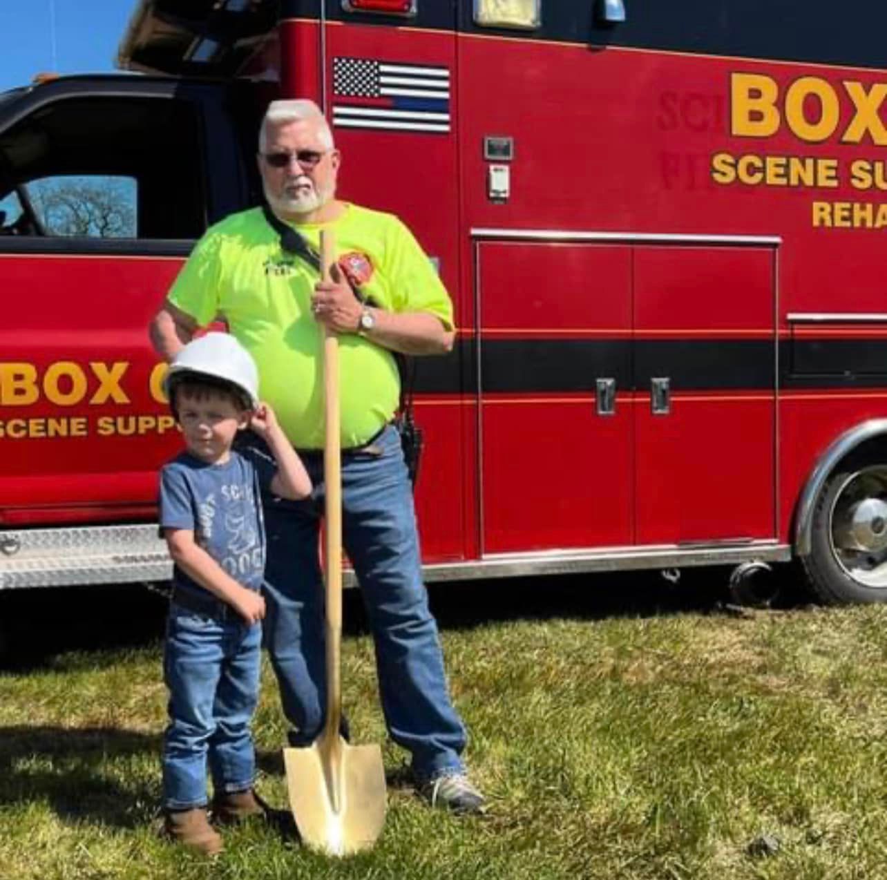 A man and a boy standing in front of a red box scene supply truck