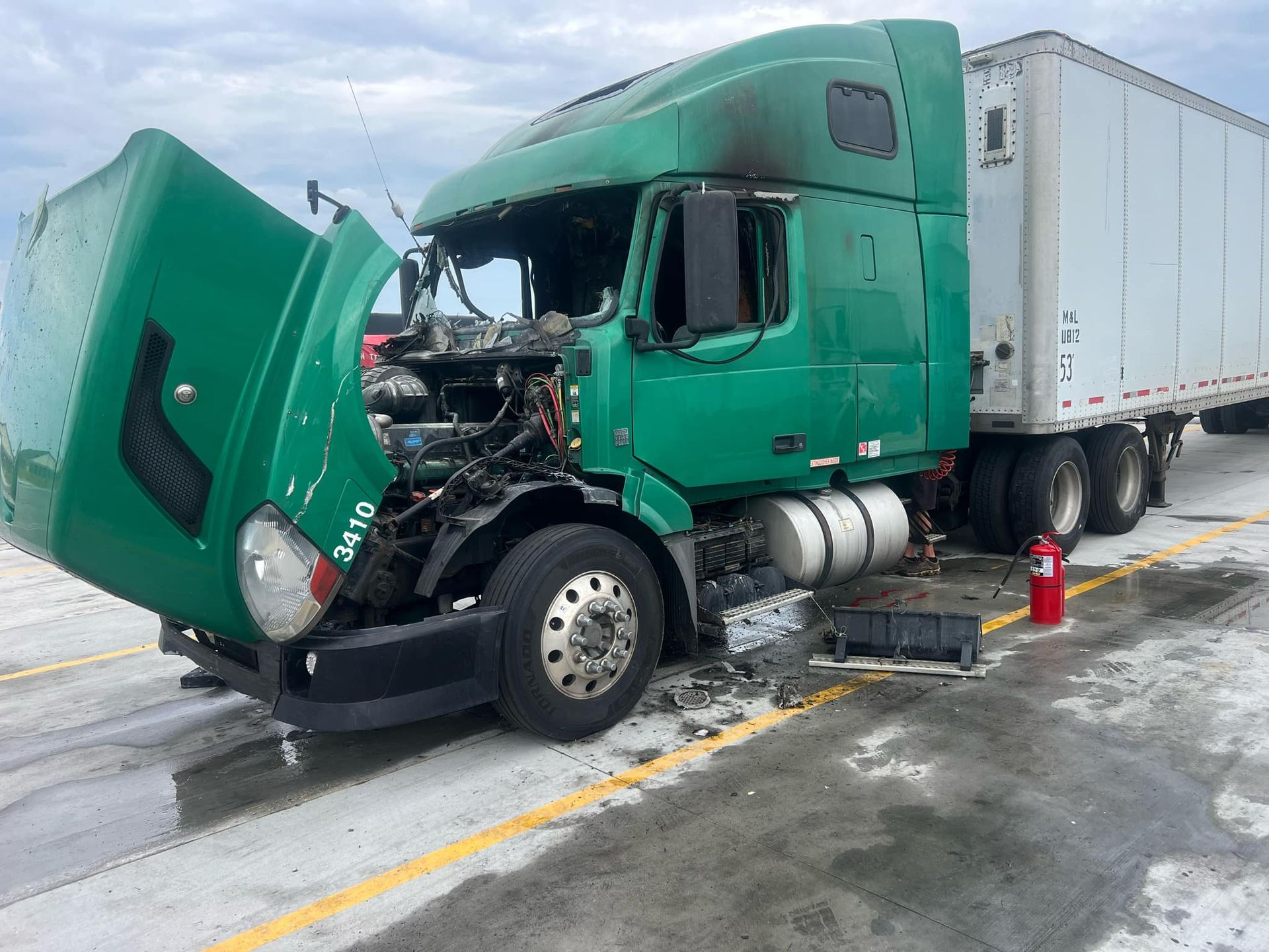 A green semi truck with its hood open is parked on the side of the road.