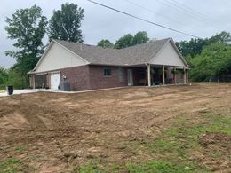 Brick house with attached garage and porch on a newly graded lot under an overcast sky.
