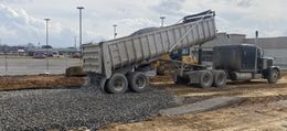 A dump truck is dumping gravel on a construction site. Cloudy sky in background.