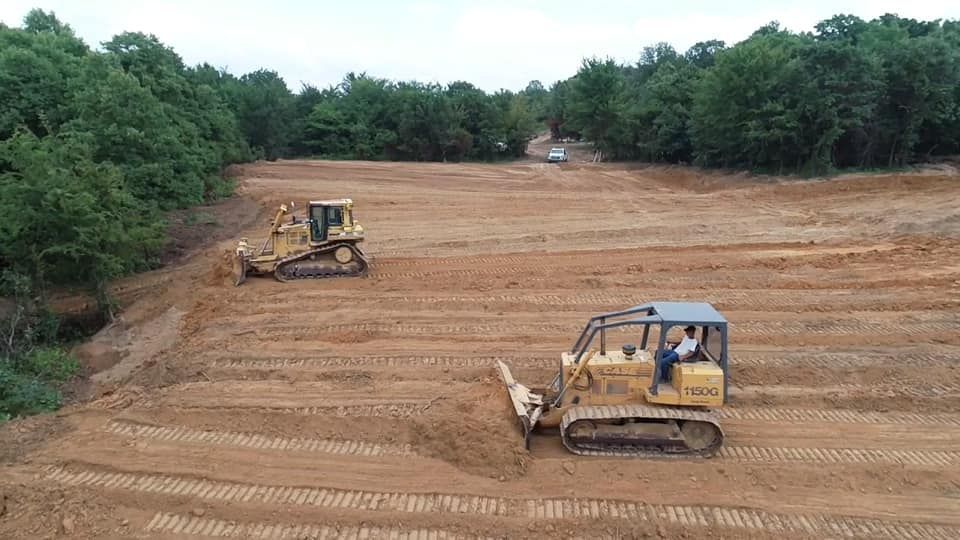 Two yellow bulldozers leveling a cleared brown field near a forest.