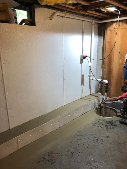 Basement utility area with white walls, exposed pipes, and a concrete floor.